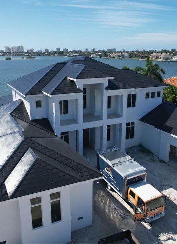 roof-contractors_florida Aerial view of a white waterfront Florida home with a new dark roof and a work truck in the driveway